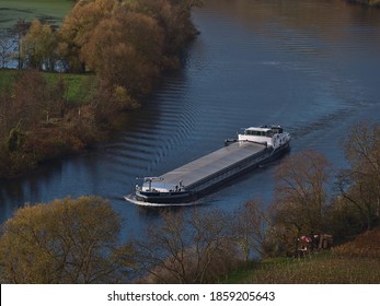 Hessigheim, Germany - 11/21/2020: Loaded barge ship (inland vessel) on Neckar River in autumn season with discolored trees and bare vineyards on the banks.