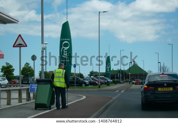 Hessle, Kingston Upon Hull, Britain - 12th May 2019:
Entrance to St Andrews Quay Retail Park, big outlet shops, free
parking. Man at work collecting rubbish and wheeling a big green
waste bin 