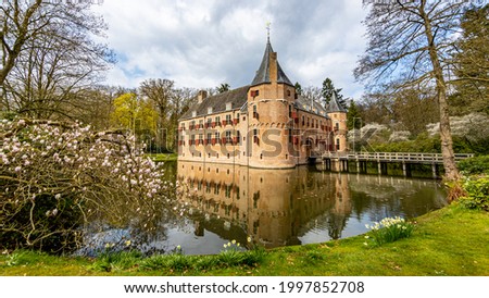 Het Oude Loo castle with its bridge, surrounded by its moat with reflection in the water and trees, sunny spring day with a blue sky and white clouds in Paleispark Kroondomein, Apeldoorn, Netherlands