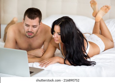 Heterosexual Couple Watching Movie On Laptop Computer In Bedroom.