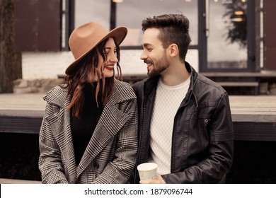 Heterosexual satisfied married couple have a date outside near cafe on pier. Drinking hot chocolate coffee beverage and hugging, kissing, speaking and laughing, spend time. Romantic lovers husband wif