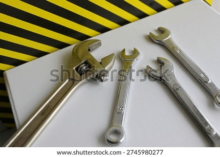 Hex wrenches and adjust spanner on a carton container near a sign with black and yellow hazard stripes
