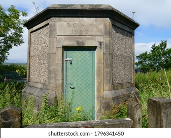 Hexagonal Concrete Pumping Station With Green Door At The Wayoh Reservoir Surrounded By Undergrowth And Weeds