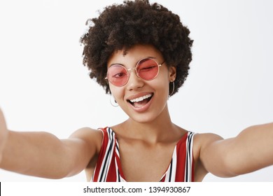 Hey, what is up. Playful hot African American with afro hairstyle, pulling hands towards camera to make selfie, winking joyfully and smiling broadly, making new profile pic for social network
