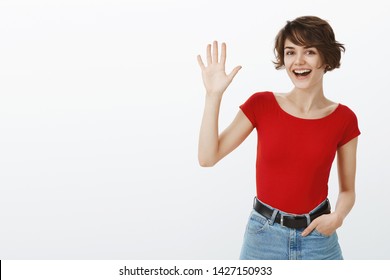 Hey Whats Up. Attractive Sociable Cheerful Friendly European Girl Short Haircut Waving Raised Palm Say Hi Hello Greeting You Welcoming Guests Stand White Background Meet New People