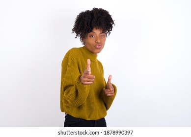 Hey you, bang. Joyful and charismatic good-looking Young beautiful African American woman wearing knitted sweater against white wall winking and pointing with finger pistols at camera happily. - Shutterstock ID 1878990397