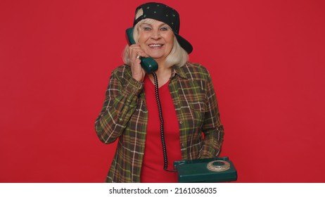 Hey You, Call Me Back. Cheerful Woman Secretary In Green Shirt Talking On Wired Vintage Telephone Of 80s, Asking New Client For Call. Elderly Grandmother Posing Isolated On Red Studio Wall Background