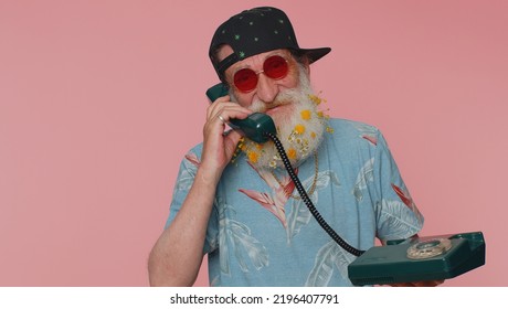 Hey You, Call Me Back. Cheerful Bearded Old Man Secretary In T-shirt Talking On Wired Vintage Telephone Of 60s, Asking New Client For Call. Elderly Grandfather Isolated On Pink Studio Wall