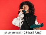 Hey you, call me. Caucasian young woman with curly hair talking on wired landline vintage telephone of 80s, advertising proposition of conversation, online shopping. Girl isolated on red background