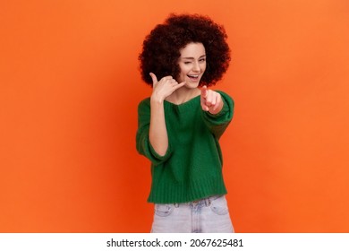 Hey You, Call Me! Woman With Afro Hairstyle Standing With Telephone Hand Gesture And Smiling To Camera, Flirting Offering To Contact By Phone. Indoor Studio Shot Isolated On Orange Background.