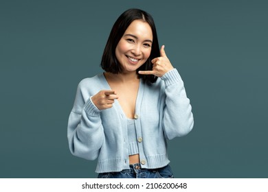 Hey You, Call Me. Woman Standing With Telephone Hand Gesture And Smiling To Camera, Flirting Offering To Contact By Phone. Indoor Studio Shot Isolated On Blue Background 