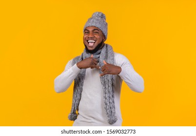 Hey you. Cheerful black winter man greeting happily at camera, yellow studio background
