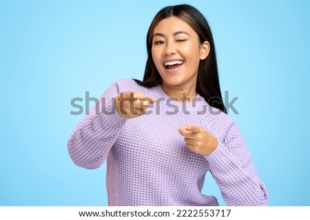 Hey you, handsome. Portrait of joyful woman winking playfully and pointing to camera, choosing guy and flirting. Indoor studio shot isolated on blue background 