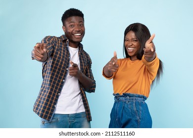 Hey, You. Portrait of cheerful African American guy and lady pointing two index fingers at camera, standing isolated over blue studio background wall. Positive young friends choosing and indicating