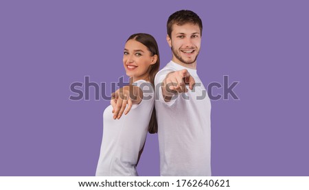 Hey, You. Portrait of cheerful casual friends pointing finger at camera, standing back to back on purple wall, copyspace