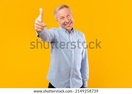 Hey, It's You. Portrait of excited mature man in checkered shirt pointing index finger at camera, posing isolated over orange yellow background wall. Cheerful guy picking, choosing and indicating
