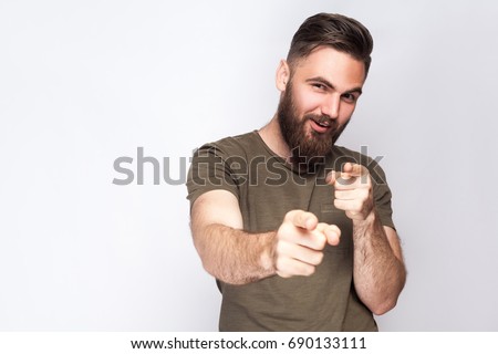 Hey you! Portrait of happy bearded man with dark green t shirt against light gray background. studio shot.  

