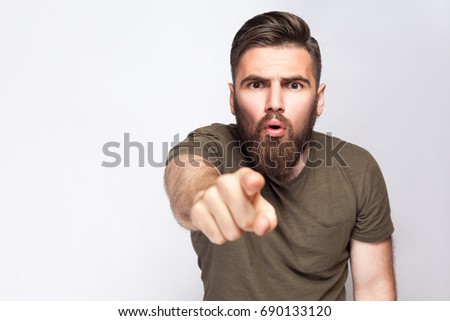 Hey You! Portrait of surprised excited bearded man with dark green t shirt against light gray background. studio shot.  
