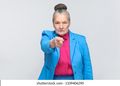 Hey you! Woman pointing at camera finger with serious face. Emotion and feelings concept. Portrait of expressive grandmother standing with collected gray hair. Studio shot, isolated on gray background