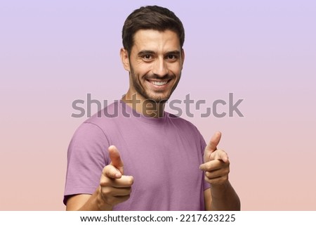 Hey you! Young man in purple t-shirt pointing to camera with fingers isolated on purple background
