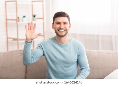 Hi. Positive Millennial Guy Waving Hello With Hand Smiling To Camera Sitting On Sofa At Home