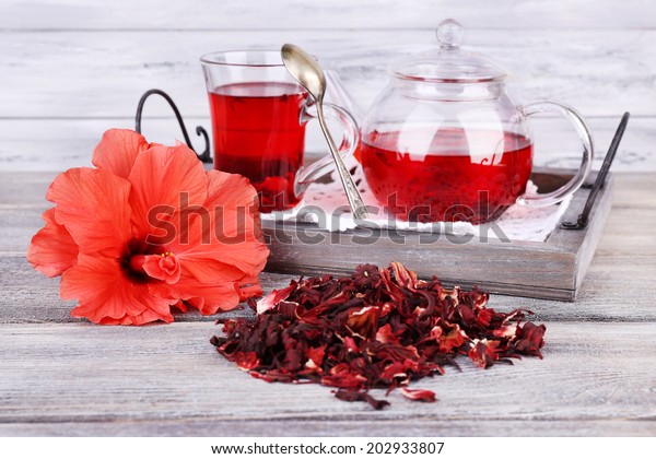 Hibiscus tea in glass teapot and flower on\
color napkin on wooden\
background
