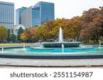 Hibiya Park, cityscape of the Grand Fountain of a park in Chiyoda city with flowing water against the coloured trees and high rise buildings during autumn in fall season in Tokyo, Japan.