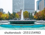 Hibiya Park, the Grand Fountain of a park in Chiyoda city with flowing water against the coloured trees and high rise buildings of the cityscape during autumn in fall season in Tokyo, Japan.