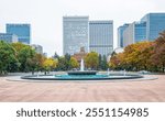 Hibiya Park, the Grand Fountain of a park in Chiyoda city with flowing water against the coloured trees and high rise buildings of the cityscape during autumn in fall season in Tokyo, Japan.