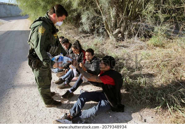 Hidalgo, TX, USA - Nov. 16,\
2021:  A Border Patrol agent hands out masks and water to a group\
of Mexicans who crossed the Rio Grande River illegally to enter the\
U.S.