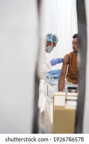 Hidden Camera View Of The Doctor In Medical Face Mask Cleaning Skin On Patient's Arm With Disinfectant Before Injection Of Flu Or Covid-19 Antivirus Vaccine, Coronavirus Concept