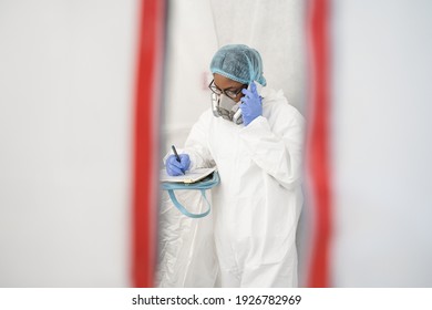 Hidden Camera View Of The Exhaustion Female Doctor Talking On A Smartphone While Having Quick Break In A Hospital Hallway During The Covid-19 Pandemic. Woman Talking And Making Some Notes