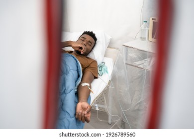 Hidden Camera View Of The Multiracial Male Patient Lying In Hospital Ward On Hospital Bed At The Isolator For Prevent The Spread Of The Virus. Coronavirus Pandemic Concept