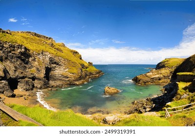 a hidden coastal cove surrounded by rugged, rocky cliffs covered in green grass. The calm, clear turquoise water gently laps against the small sandy beach at the base of the cliffs. - Powered by Shutterstock