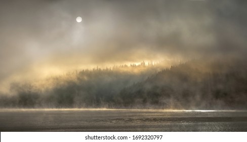 Hidden light behind mist over mountain lake and forest