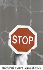 Hidden Person Holds Big Stop Road Sign. Bold Red Against Cracked Gray Wall. Fun Eye-catching Image To Represent Abstract Concepts Like Boundaries And Consent; Address Toxic Behavior And Negativity.