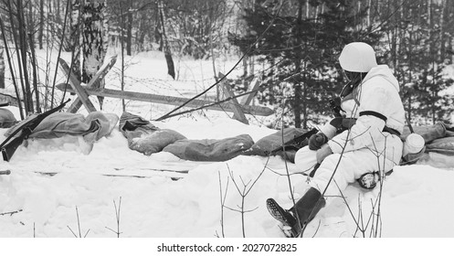 Hidden Re-enactor Dressed As German Wehrmacht Infantry Soldier In World War II Soldiers Sitting In Ambush In Winter Forest. Historical Re-enactment. WWII. Winter Snowy Day. Black And White Photo.