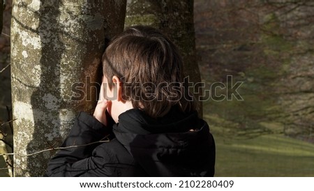      hide and seek, the boy counts next to the tree, raising his hands to his eyes                        