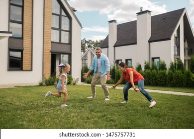 Hide And Seek. Parents And Daughter Feeling Cheerful While Playing Hide And Seek Outside Near House