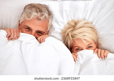 Hiding, portrait and a senior couple in bed for comfort, sleep or love in retirement. Shy, intimate and an elderly man and woman in the bedroom of a house with a blanket covering head in marriage - Powered by Shutterstock