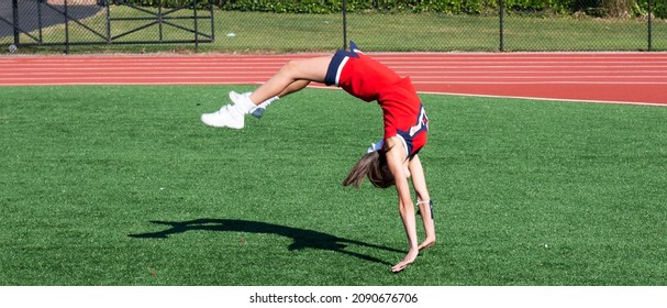 A hifh school cheerleader is upside down as she practices her running tumbling on a turf field.