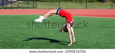 A hifh school cheerleader is upside down as she practices her running tumbling on a turf field.