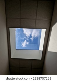 high above the head is a rectangular window illuminating the entire area of the hall with natural light. the window is a rectangular skylight. the walls are pure white plaster