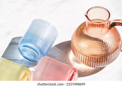 High Above View Of Jug Of Water And Colored Transparent Glasses. Kitchen Tableware Flat Lay. Minimalism Style. Home Comfort. Objects Composition