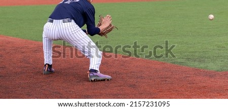 A high achool third baseman fielding a ground ball during a game close up.