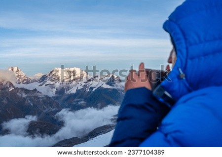 High altitude female mountaineer dressed blue warm dawn jacket holding metal mug of hot tea and drinking warm drink with Kangchenjunga mountain panorama. Mera Peak High Camp 5700m, Himalayas, Nepal.