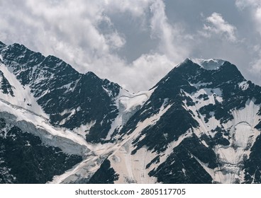 High altitude mountain range featuring steep, dark rock faces covered with extensive snow and ice.