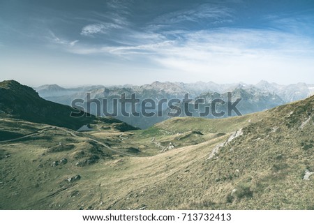 High altitude pasture, rocky mountain peaks and jagged ridge, with scenic sky, the Italian Alps. Expansive view in backlight. Toned desaturated image.