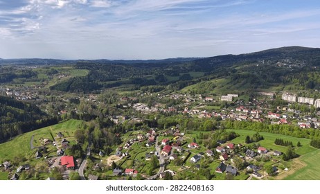 High altitude view showing patchwork fields, hedged meadows, winding roads, clustered homes, forests, and distant hills across peaceful rural countryside under bright clear sky, with aerial, panorama