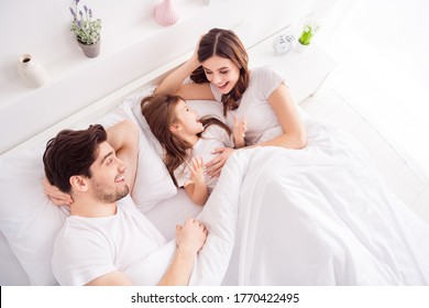 High angle above view photo of young family mommy daddy daughter lying sheets under white blanket good mood spend time chatting quarantine weekend morning self isolation bedroom indoors